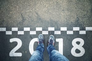 Person standing in front of a start New Year 2018 sign painted on asphalt city street. Point of view perspective used.
